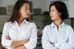 Two Asian businesswomen looking at each other in office